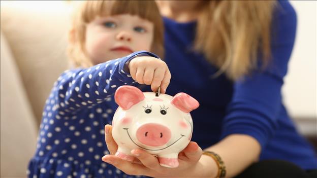 Young girl putting a coin in piggy bank